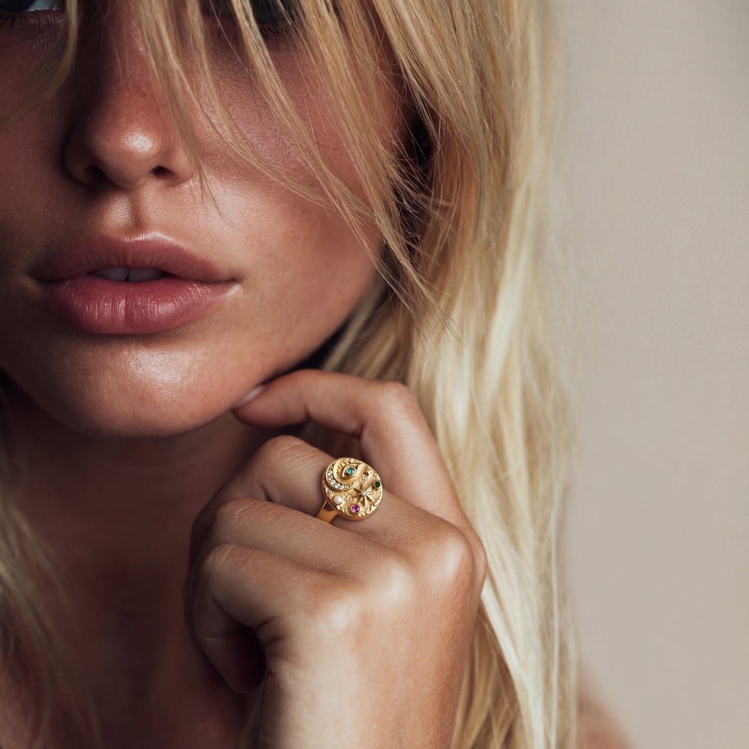 Close-up of a woman wearing a gold ring with a gemstone, against a neutral background.