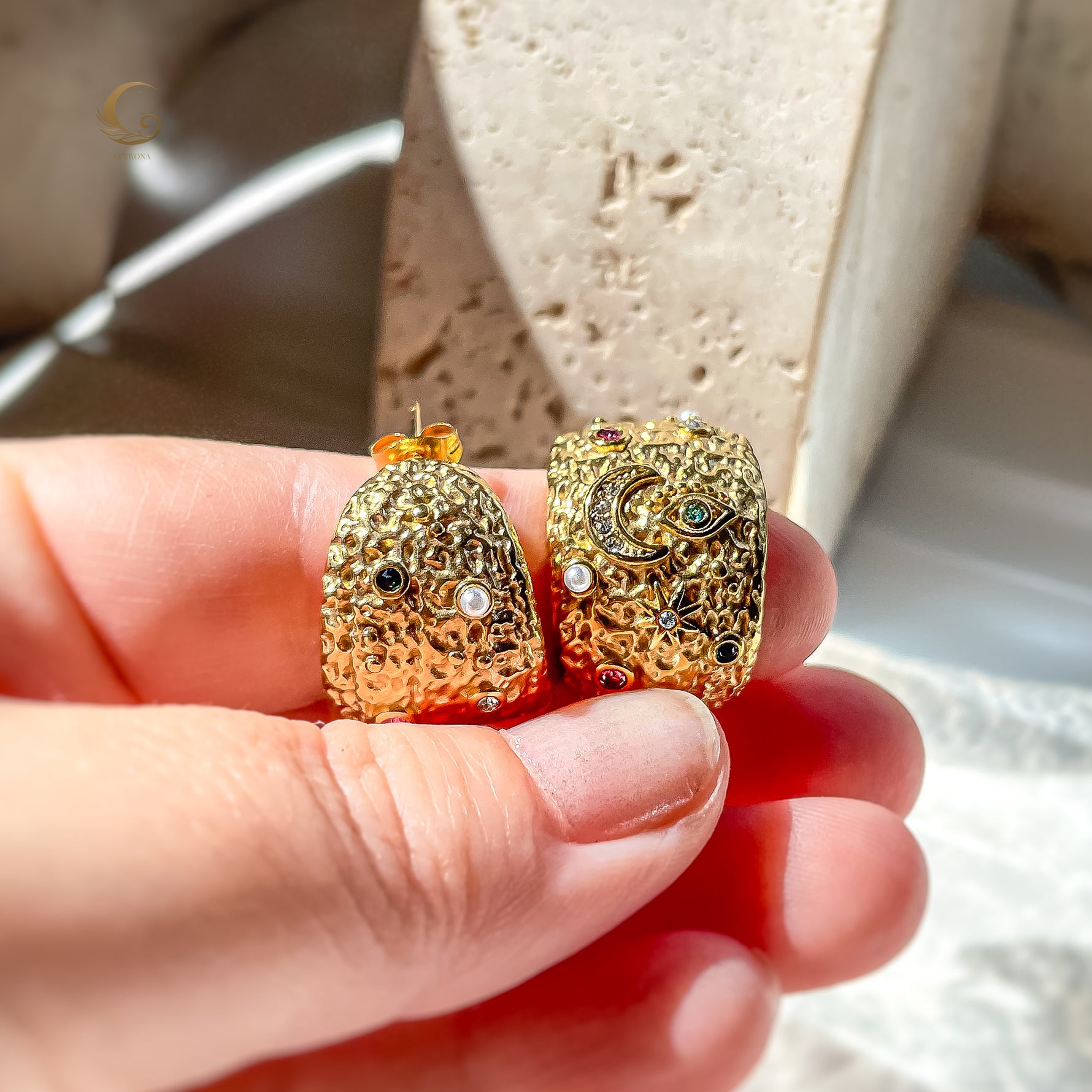 Gold moon and evil eye earrings shown in hand for size reference, showcasing rich texture and colorful crystal accents.