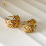 Overhead view of large celestial hoop earrings with detailed surface and starry elements, placed on white background.