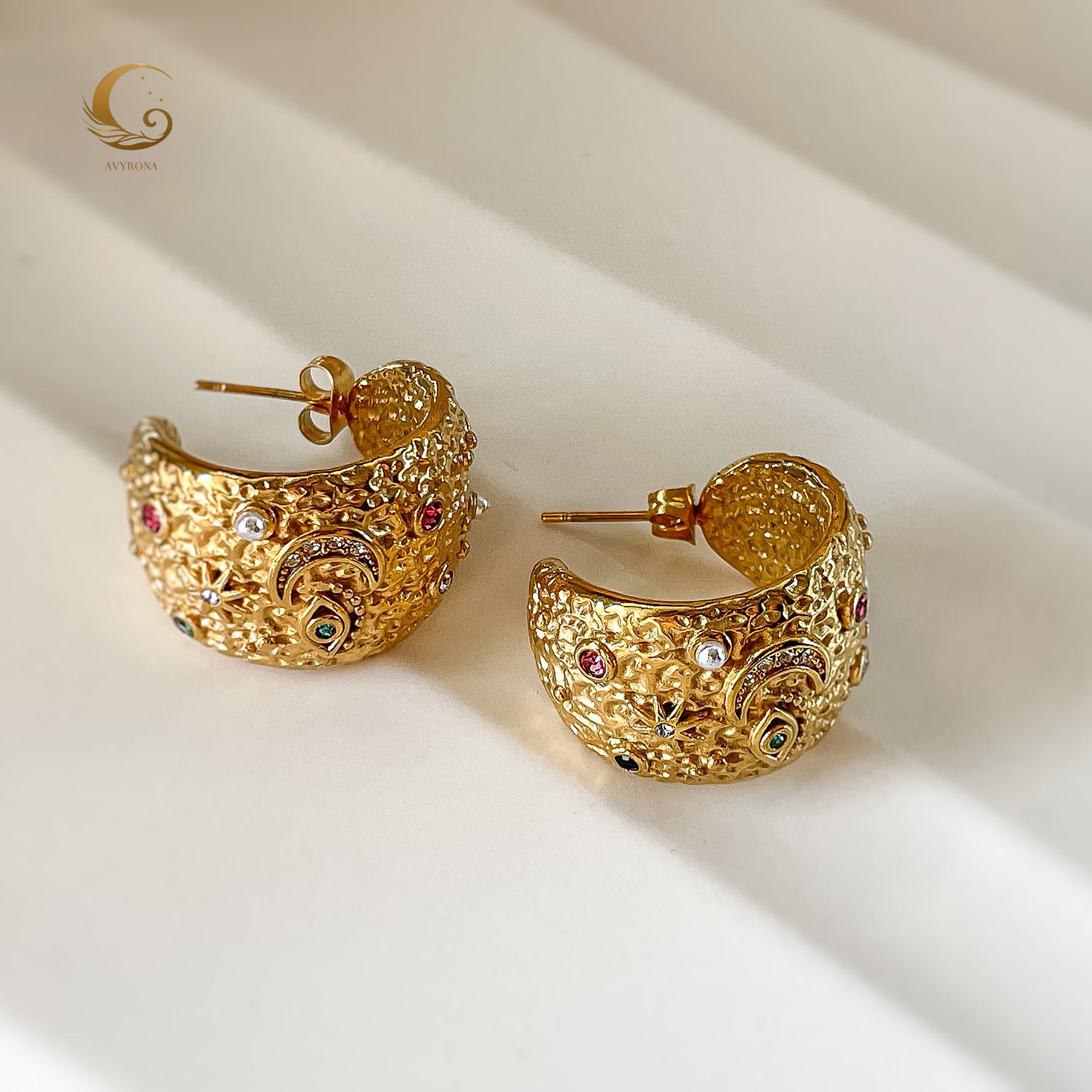 Overhead view of large celestial hoop earrings with detailed surface and starry elements, placed on white background.