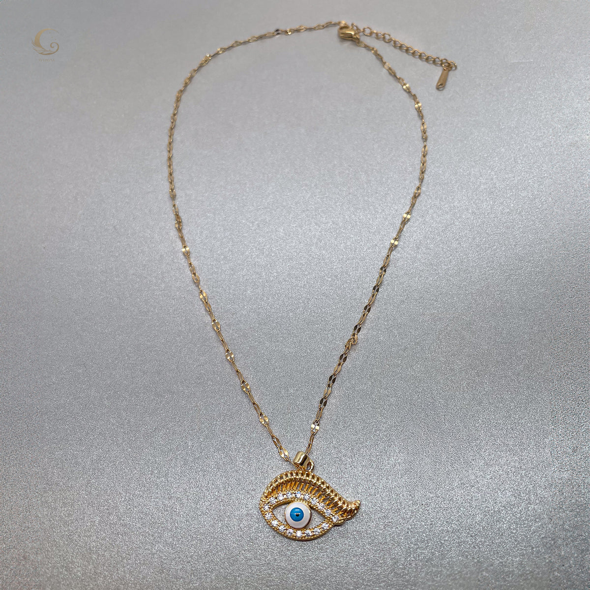 Full view of gold evil eye necklace with twisted chain and lobster clasp, laid flat on silver background, celestial style by Avyrona