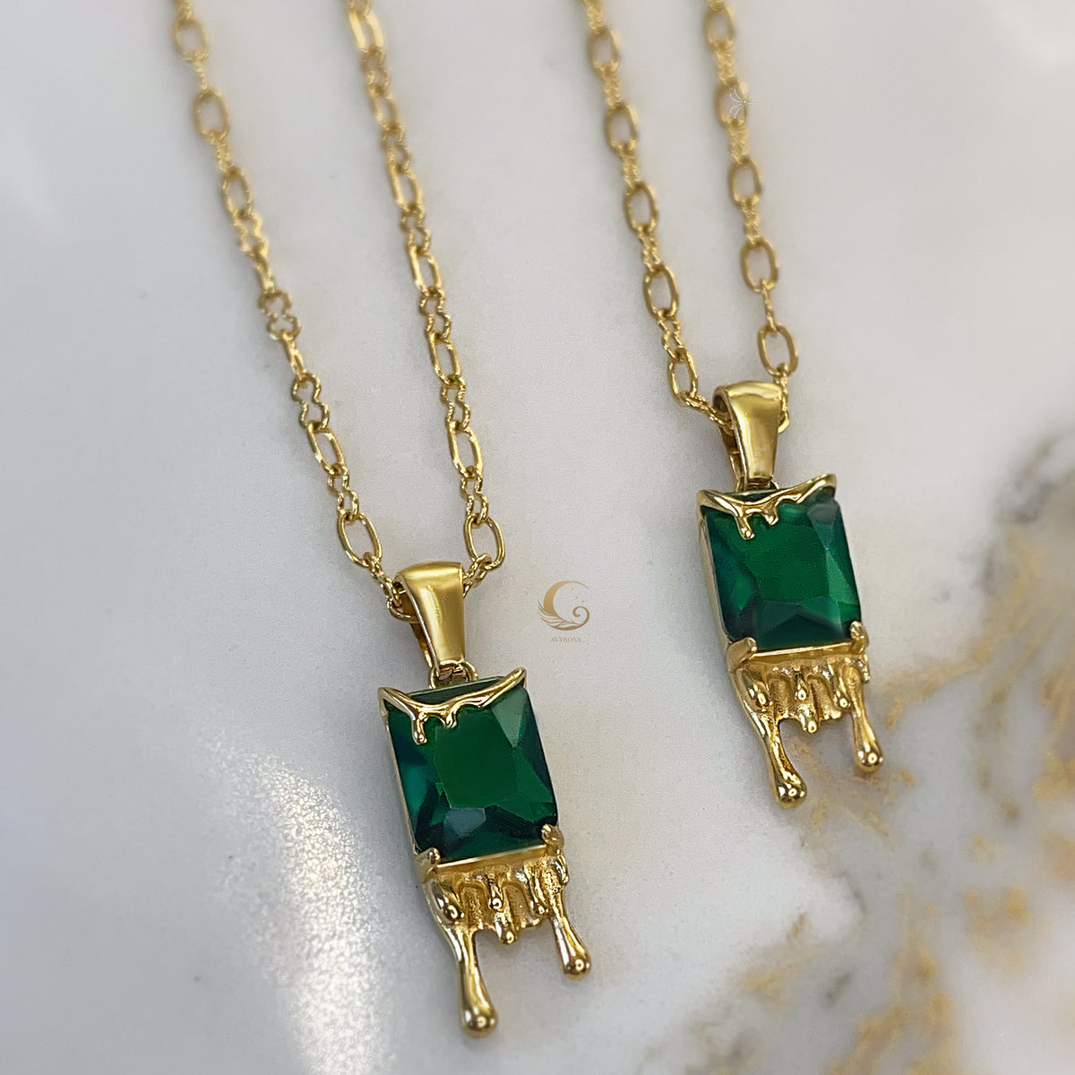  Pair of Mila necklaces displayed artistically, emphasizing unique honey drip feature and deep green crystals.