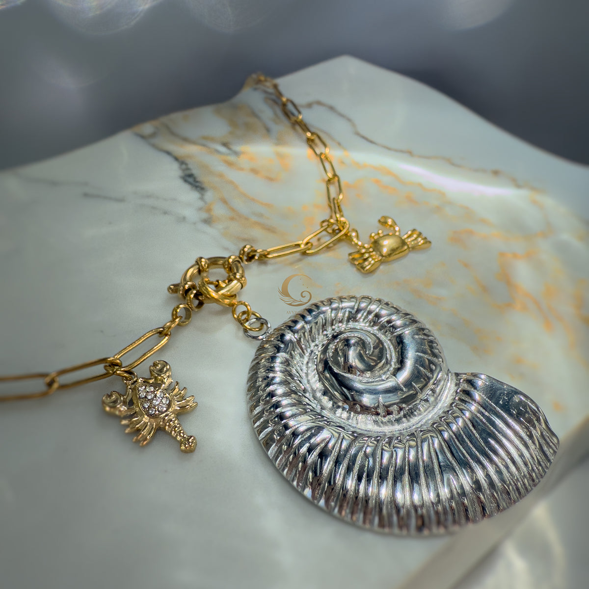  Close-up of Nerida necklace with silver shell, golden crab and lobster charms on marble background