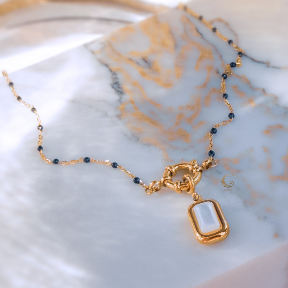Close-up of navy blue beaded necklace with rectangular mother of pearl pendant and gold toggle clasp, placed on marble background
