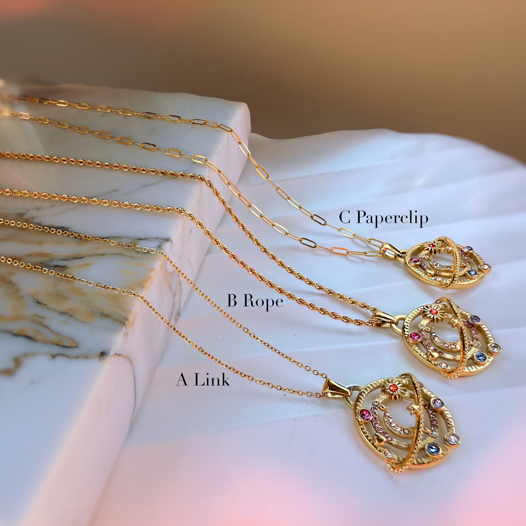 Gold celestial moon necklaces labeled A Link, B Rope, and C Paperclip, displayed on marble stone surface.
