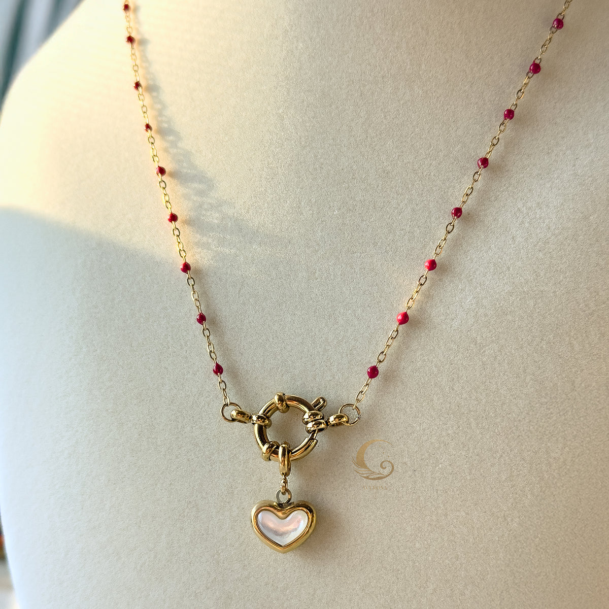  Close-up of red beaded necklace with heart charm and toggle clasp shown on bust against soft light background