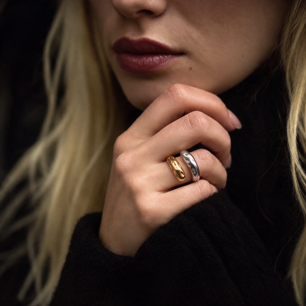 A close-up of a woman's hand wearing two slim bands rings, one in yellow gold and one in silver, against a dark background.