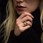 A close-up of a woman's hand wearing two slim bands rings, one in yellow gold and one in silver, against a dark background.