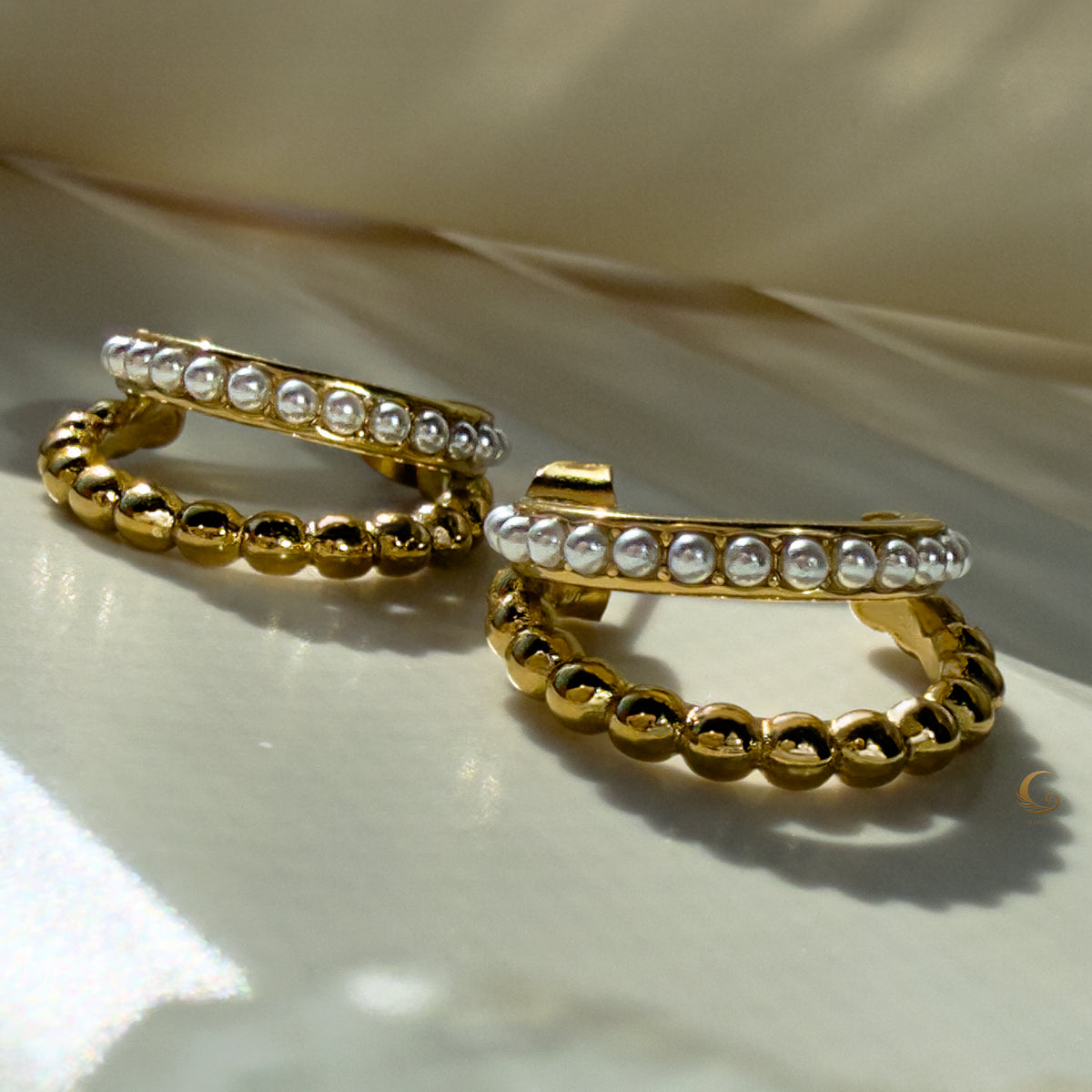 Elevated view of Serina hoop earrings resting on curved display, revealing structure and shine