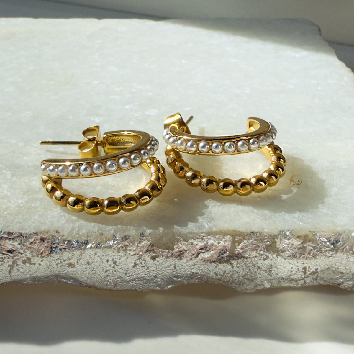 Serina earrings placed on textured stone background, showing layered pearl and gold details