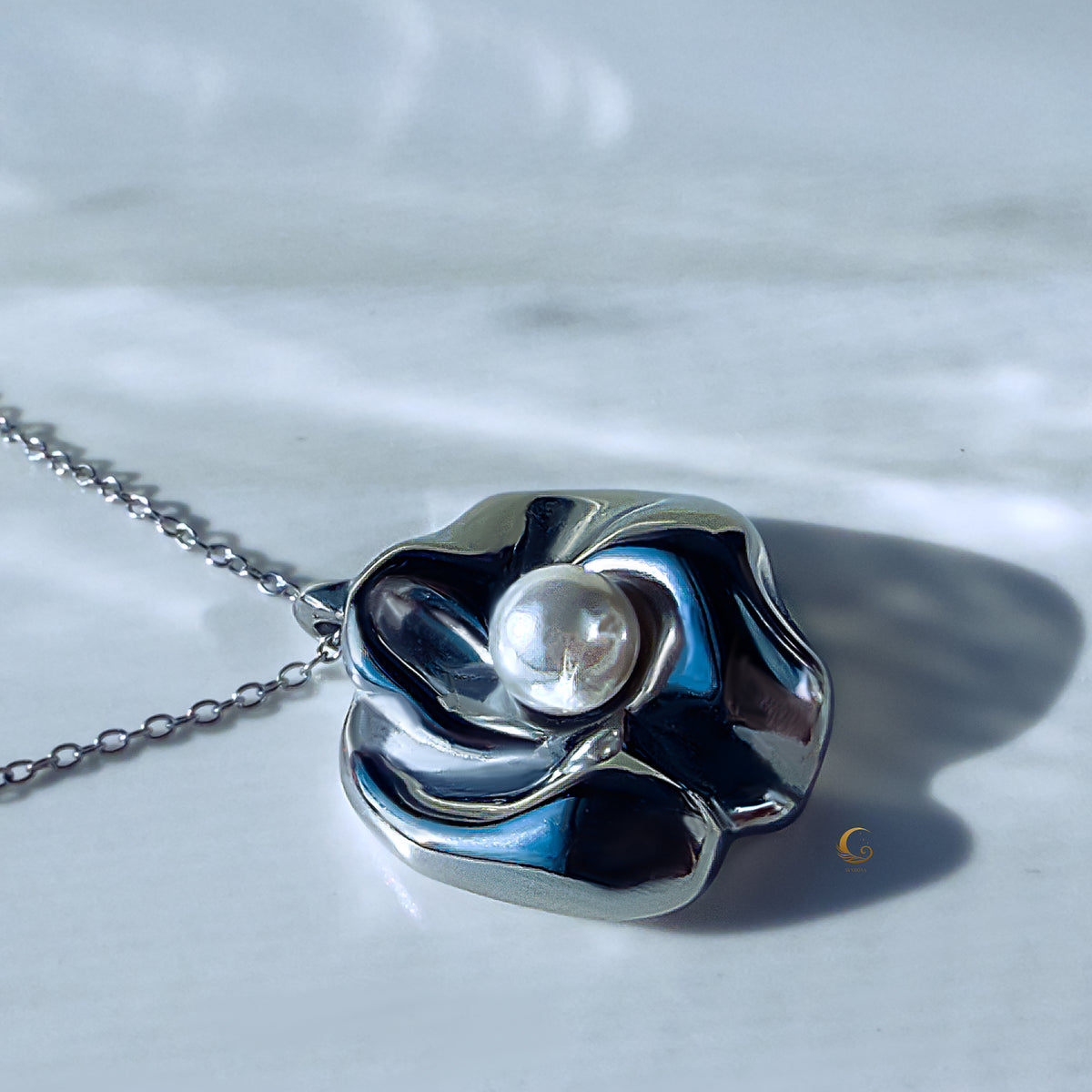 Close-up of silver sculpted flower pendant with pearl and soft shadow