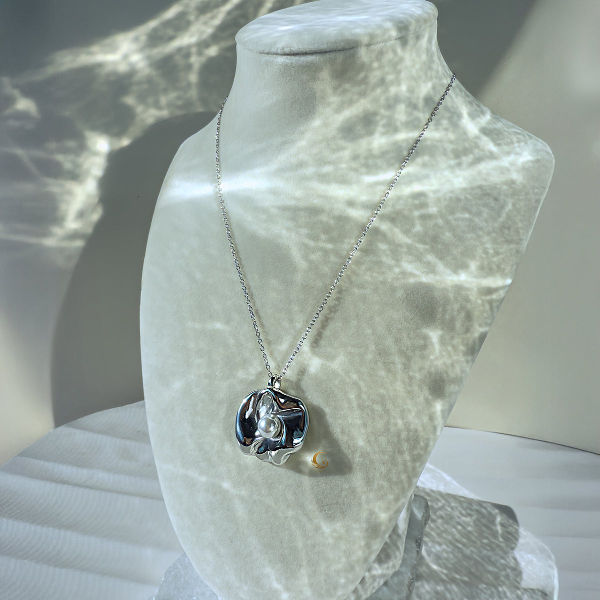 Silver flower necklace with pearl displayed on a jewelry bust with light reflections