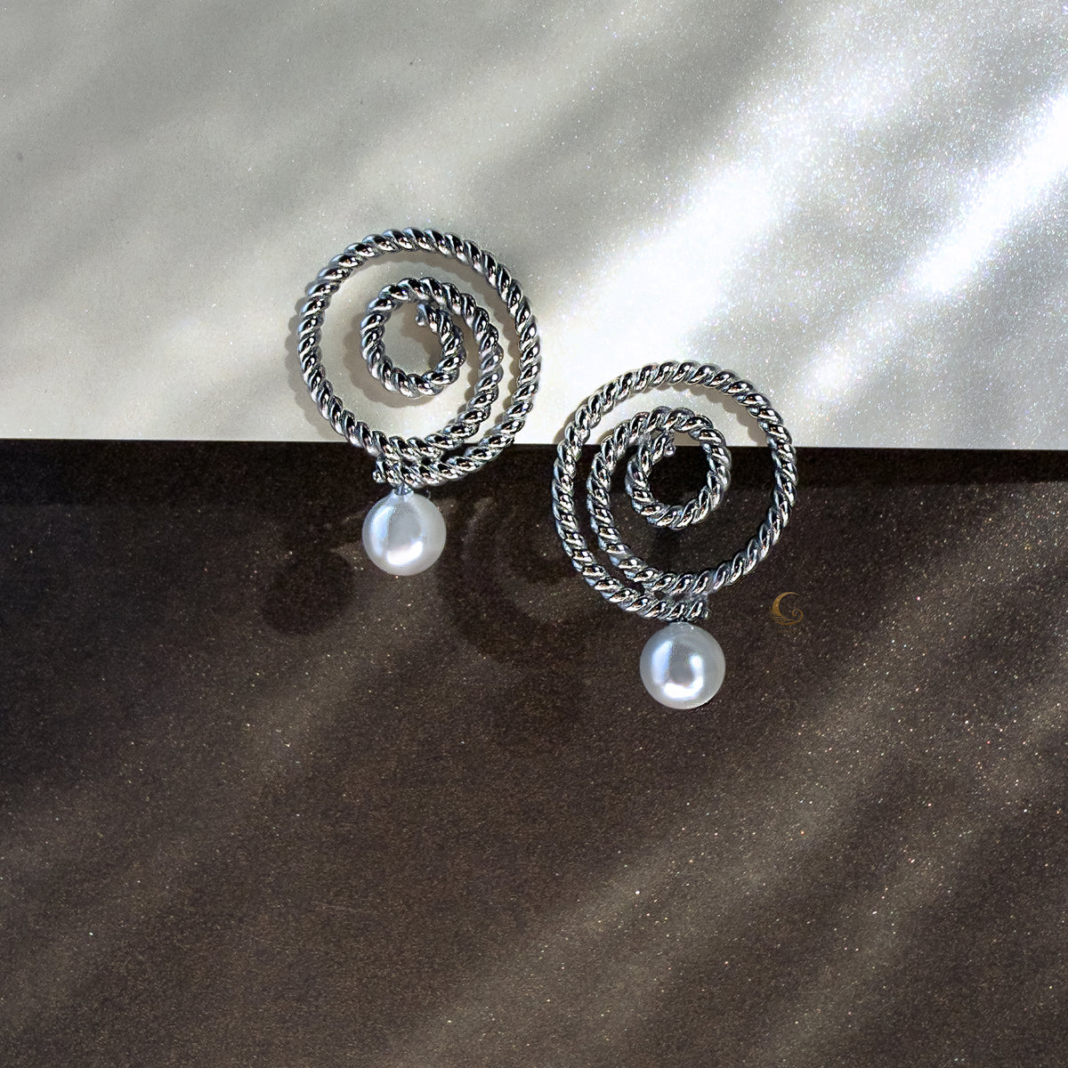 Silver Thaleia spiral earrings with pearl-like beads against dark shimmering background