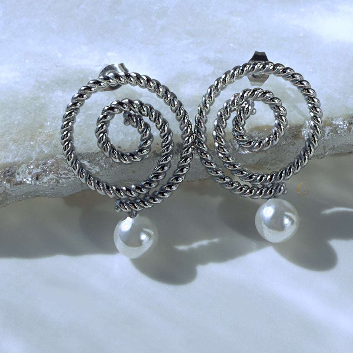 Thaleia silver spiral earrings with pearl-like drops on icy crystal surface