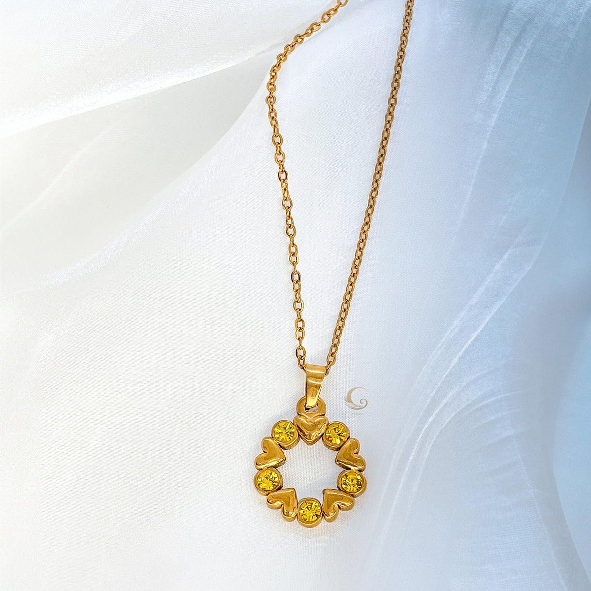 Close-up of Solara necklace pendant, golden hearts and yellow stones forming a circle, laying on light background