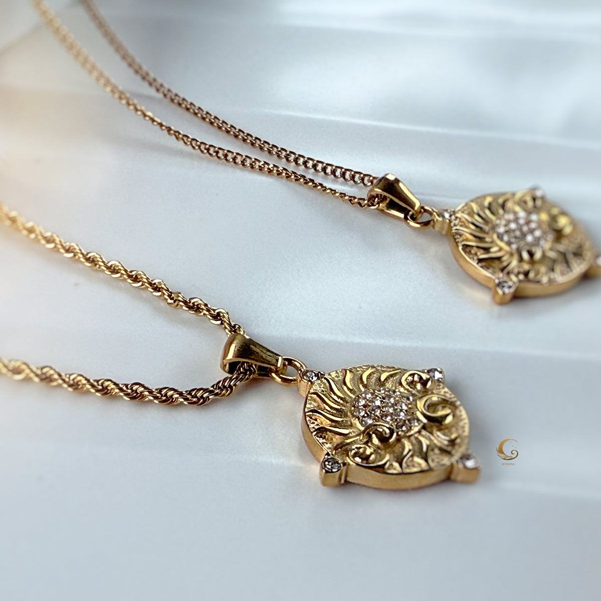 Close-up of two Soleia pendants resting on satin — golden sun charms with sparkling centers