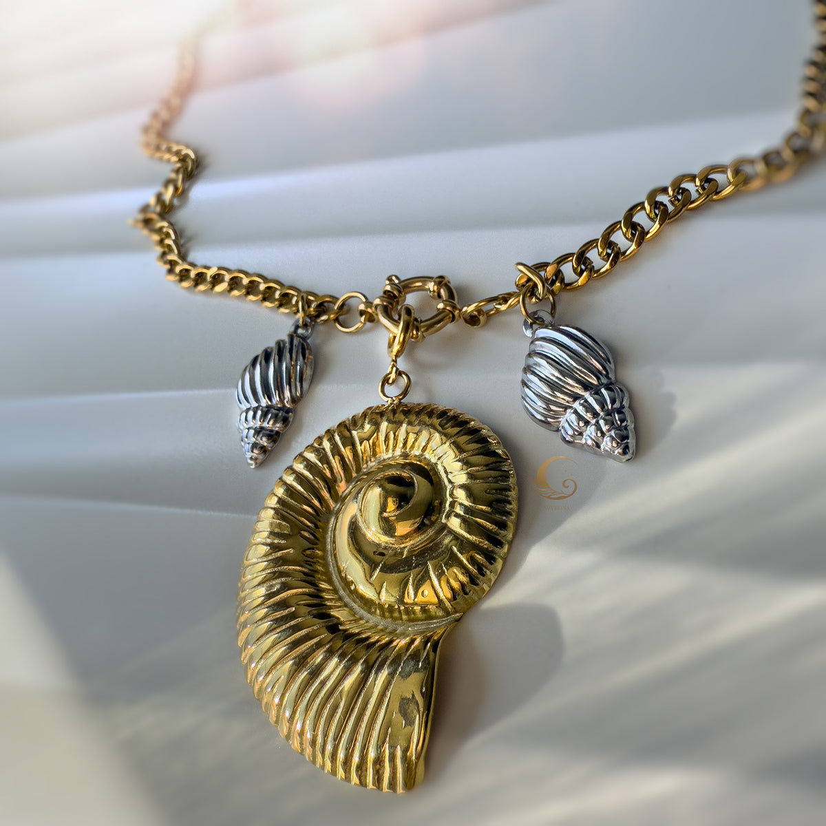 Front view of the Thalassa necklace highlighting the bold gold spiral shell and detailed silver charms, captured in soft natural light.
