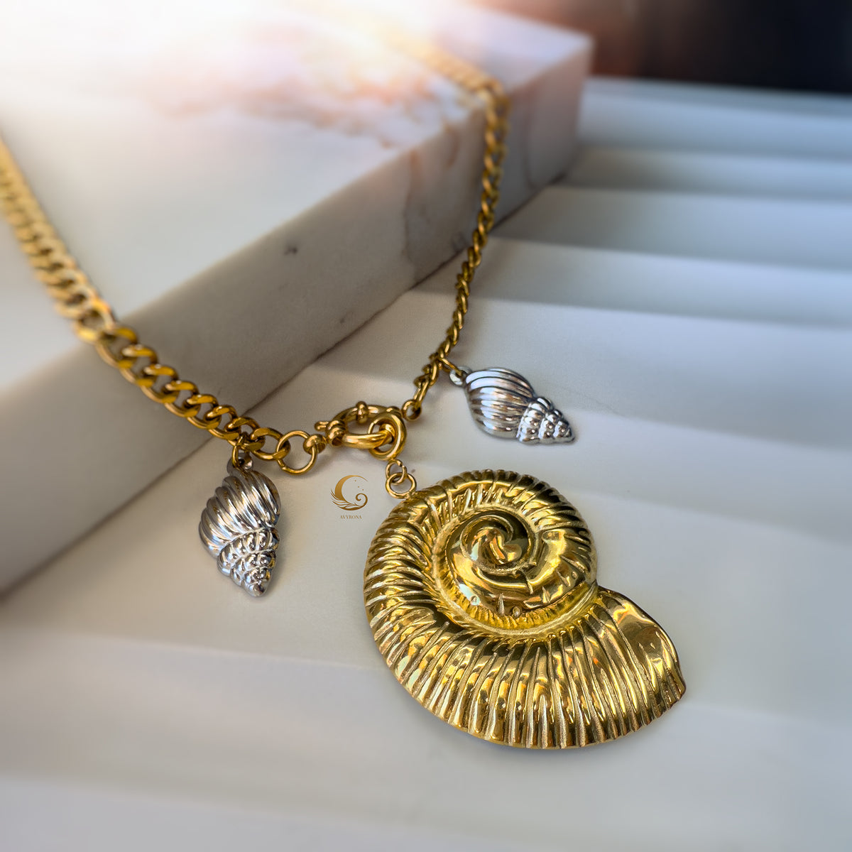 Thalassa necklace styled on a marble block, emphasizing the contrast of gold and silver against a soft pink stone.