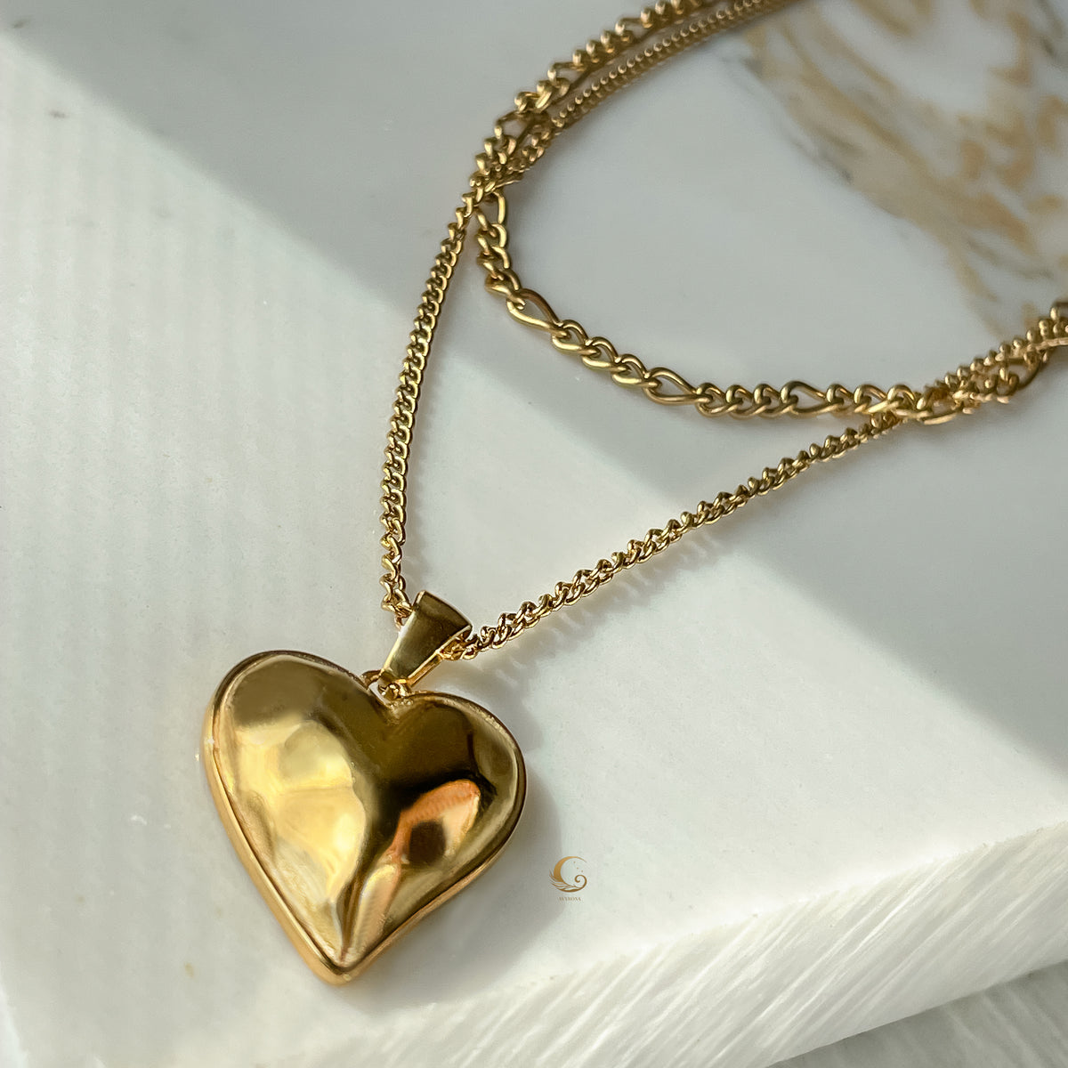 Gold layered heart necklace with double chains displayed on marble background in warm sunlight, showing vintage sculptural pendant.