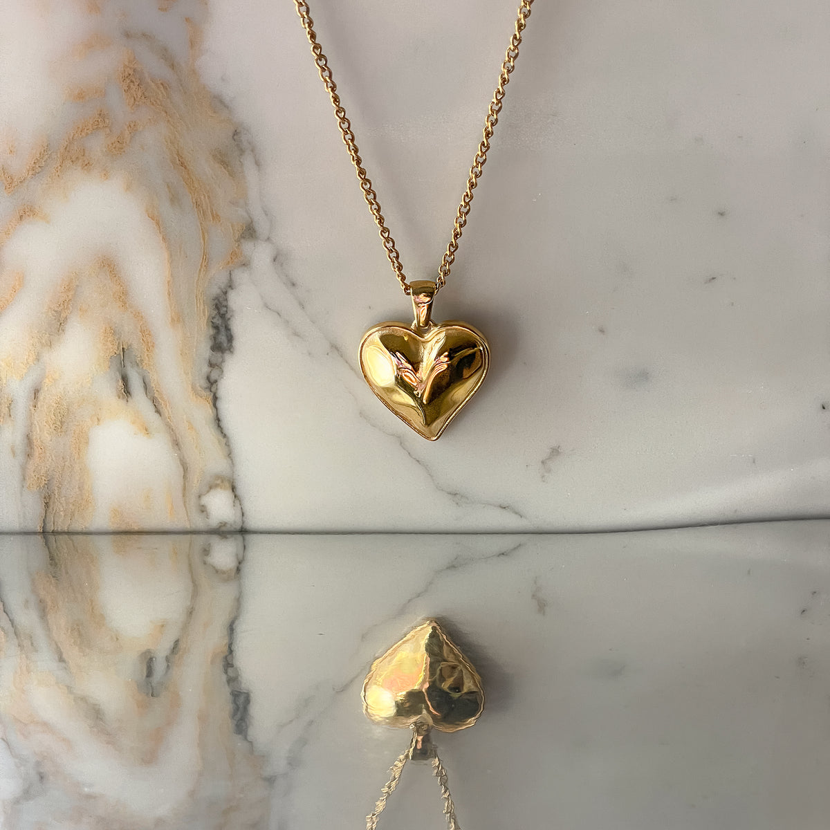 Vintage gold heart necklace with layered chains captured vertically on polished marble surface with soft shadow and reflection.