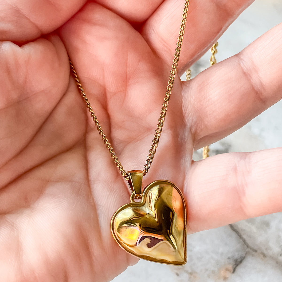 Gold heart necklace held in hand, showcasing its warm glow and feminine charm in natural daylight.